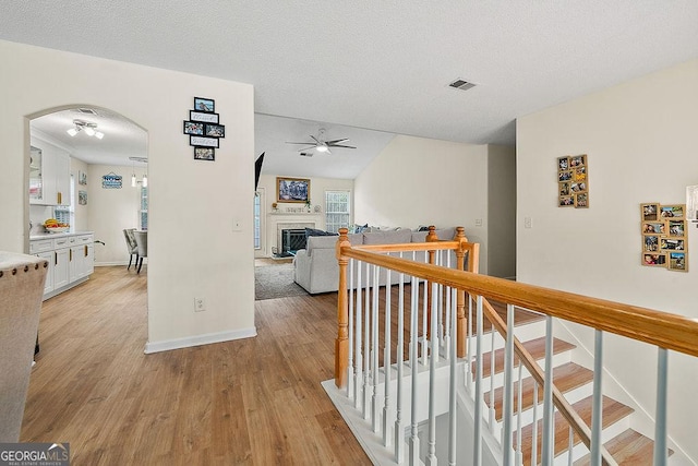 hall with arched walkways, visible vents, light wood-style floors, a textured ceiling, and baseboards