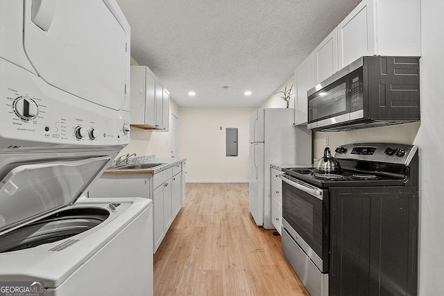 kitchen with stacked washer and clothes dryer, stainless steel appliances, light countertops, white cabinets, and electric panel