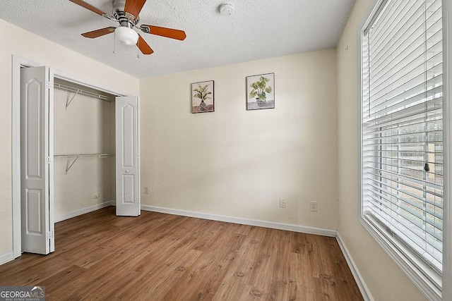 unfurnished bedroom with light wood finished floors, a closet, a ceiling fan, a textured ceiling, and baseboards