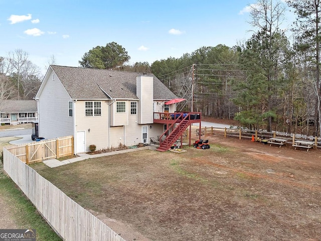 back of property with a chimney, a lawn, a deck, a fenced backyard, and stairs