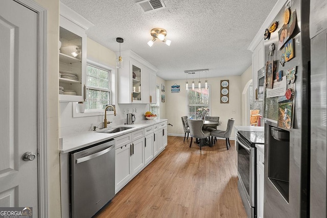 kitchen with pendant lighting, stainless steel appliances, light countertops, glass insert cabinets, and a sink