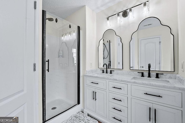 bathroom featuring a sink, a shower stall, a textured ceiling, and double vanity