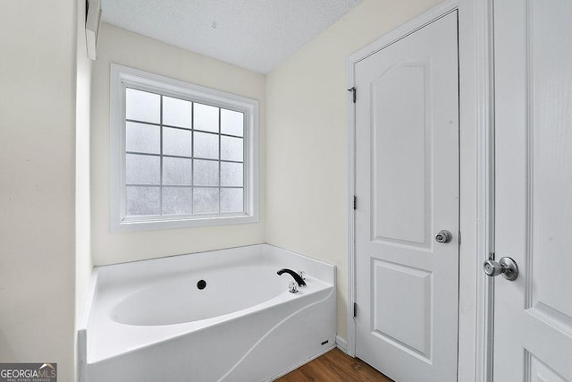 full bathroom featuring a garden tub, a textured ceiling, and wood finished floors