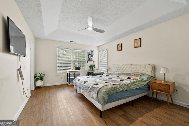 bedroom featuring visible vents, a textured ceiling, a tray ceiling, and wood finished floors