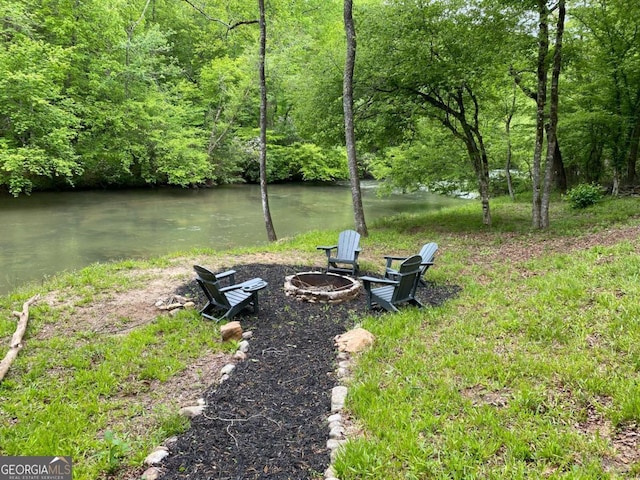 view of yard featuring a fire pit, a forest view, and a water view