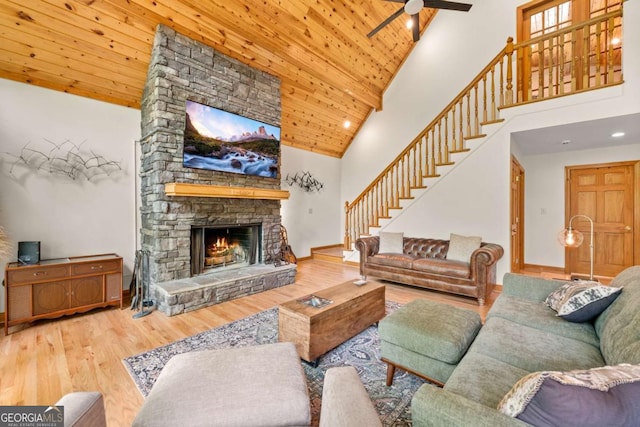 living room featuring wooden ceiling, stairway, wood finished floors, a stone fireplace, and high vaulted ceiling