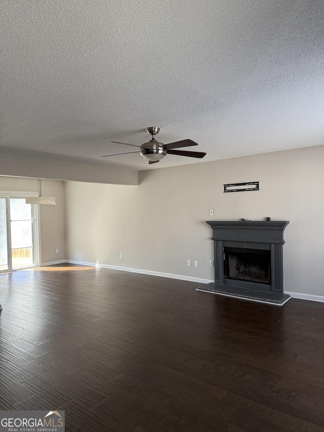 unfurnished living room featuring dark wood-style flooring, a fireplace with raised hearth, ceiling fan, and baseboards