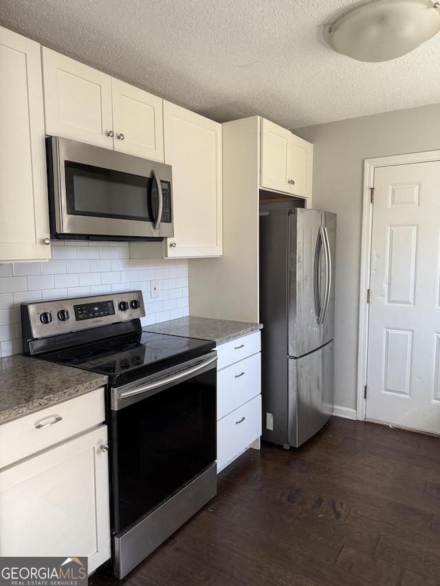 kitchen with dark wood-style floors, stainless steel appliances, dark countertops, tasteful backsplash, and white cabinetry