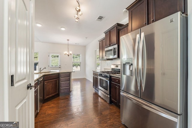 kitchen featuring light stone counters, dark brown cabinetry, stainless steel appliances, visible vents, and hanging light fixtures