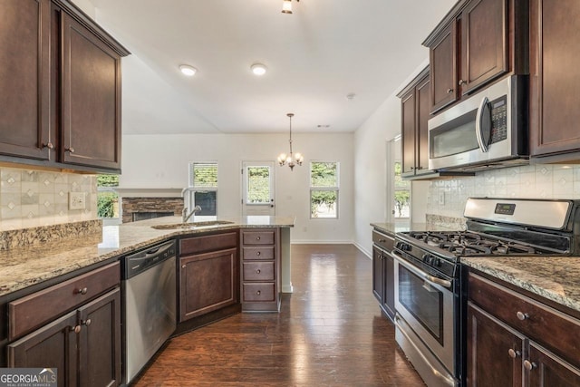 kitchen featuring appliances with stainless steel finishes, a sink, light stone countertops, and pendant lighting