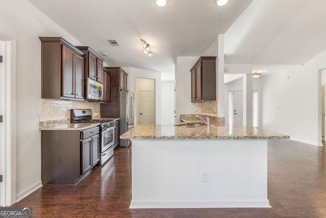 kitchen featuring stainless steel appliances, visible vents, a sink, light stone countertops, and a peninsula