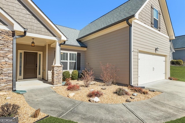 entrance to property with an attached garage, stone siding, a shingled roof, and concrete driveway