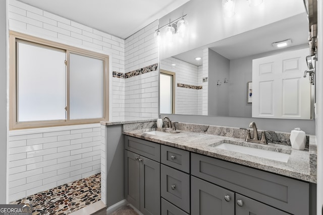 bathroom featuring a wealth of natural light, tiled shower, a sink, and double vanity