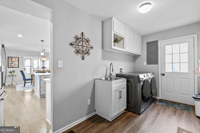 clothes washing area with dark wood-style flooring, a sink, washer and dryer, electric panel, and cabinet space