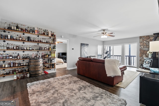 living room featuring a wood stove, ceiling fan, a bar, and dark wood-style flooring