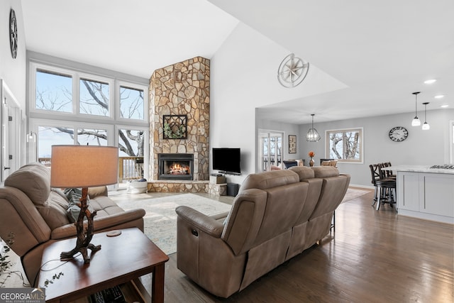 living room featuring dark wood finished floors, a stone fireplace, high vaulted ceiling, a notable chandelier, and recessed lighting