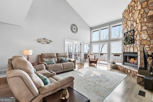 living room with french doors, a stone fireplace, high vaulted ceiling, and wood finished floors