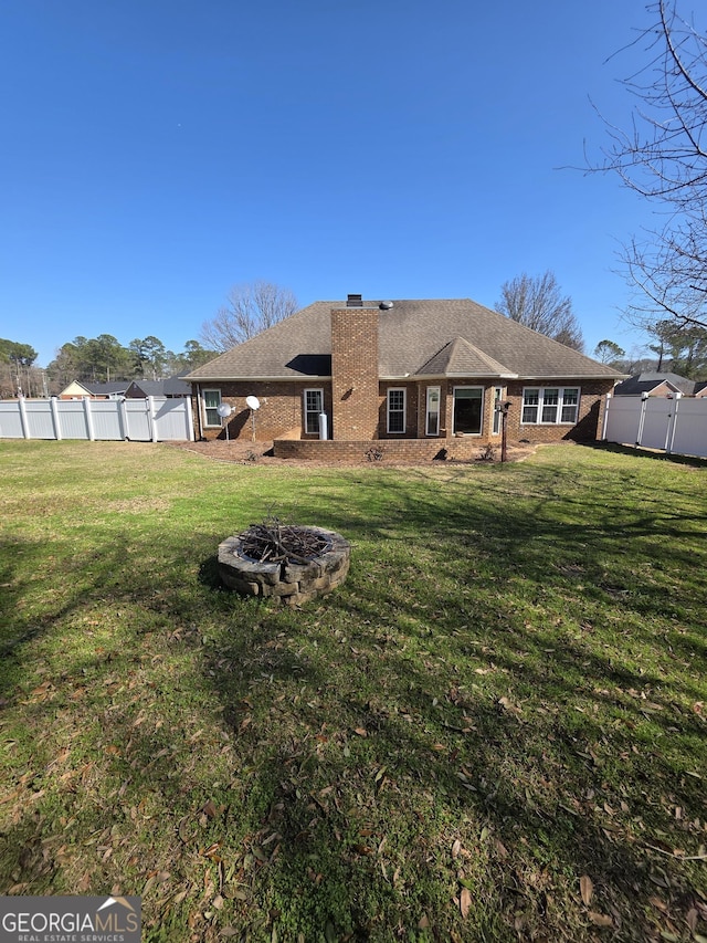 back of property featuring fence, a fire pit, and a yard