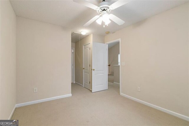 unfurnished bedroom with light colored carpet, attic access, baseboards, and ceiling fan