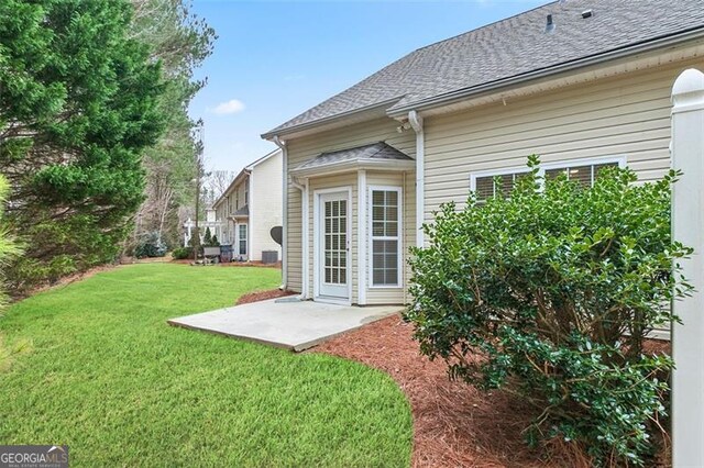 rear view of property featuring a lawn, roof with shingles, and a patio area