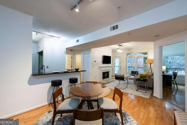 dining space featuring a fireplace with flush hearth, baseboards, visible vents, and light wood finished floors