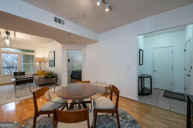 dining room featuring baseboards, rail lighting, visible vents, and light wood-style floors