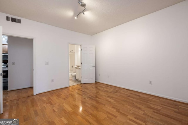 unfurnished bedroom with light wood-type flooring, ensuite bath, baseboards, and visible vents