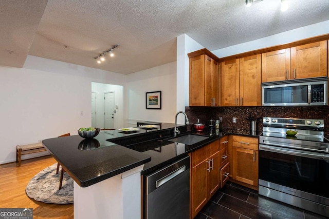 kitchen with appliances with stainless steel finishes, brown cabinetry, a sink, dark stone countertops, and a peninsula