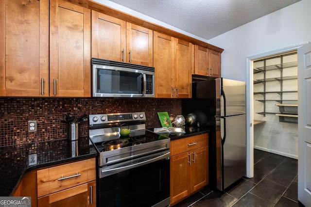 kitchen with stainless steel appliances, brown cabinets, dark tile patterned floors, and decorative backsplash