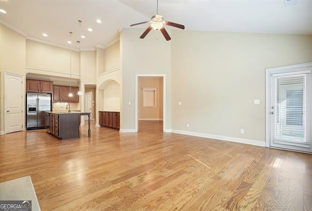 unfurnished living room featuring light wood finished floors, ceiling fan, baseboards, and arched walkways