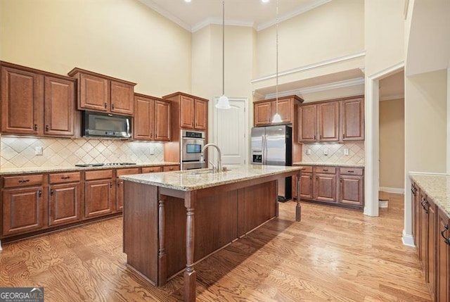 kitchen featuring light stone counters, a breakfast bar area, stainless steel appliances, a center island with sink, and pendant lighting