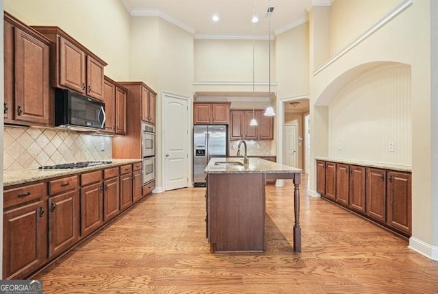 kitchen featuring appliances with stainless steel finishes, a kitchen island with sink, crown molding, and light stone counters