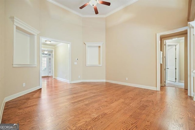 interior space featuring baseboards, a ceiling fan, ornamental molding, a high ceiling, and light wood-style floors