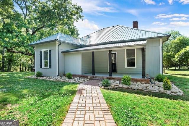 view of front of property with metal roof, a porch, a chimney, and a front yard