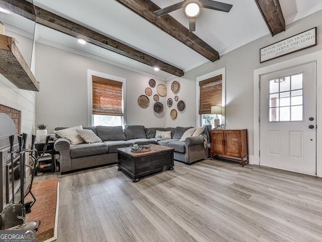 living area featuring light wood-type flooring, beamed ceiling, plenty of natural light, and a brick fireplace