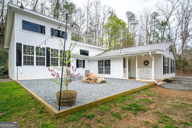 rear view of property with board and batten siding, an outdoor fire pit, a sunroom, and metal roof