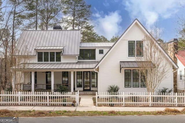 modern inspired farmhouse with a fenced front yard, a chimney, a porch, a standing seam roof, and metal roof