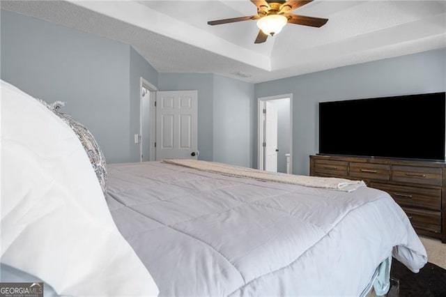 carpeted bedroom with a raised ceiling and a ceiling fan