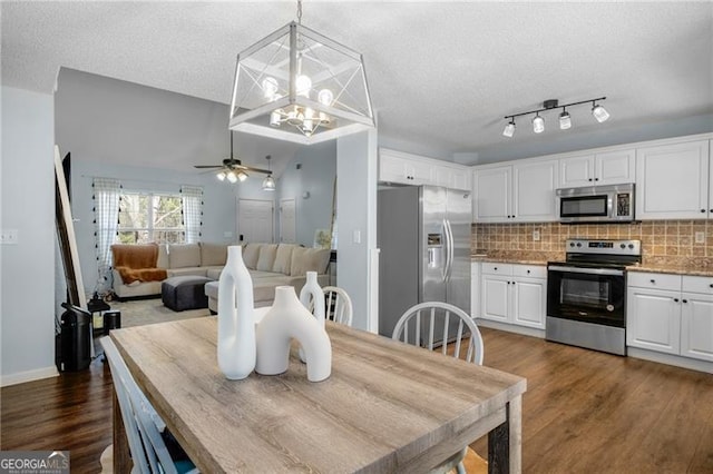 interior space with white cabinets, open floor plan, appliances with stainless steel finishes, backsplash, and pendant lighting