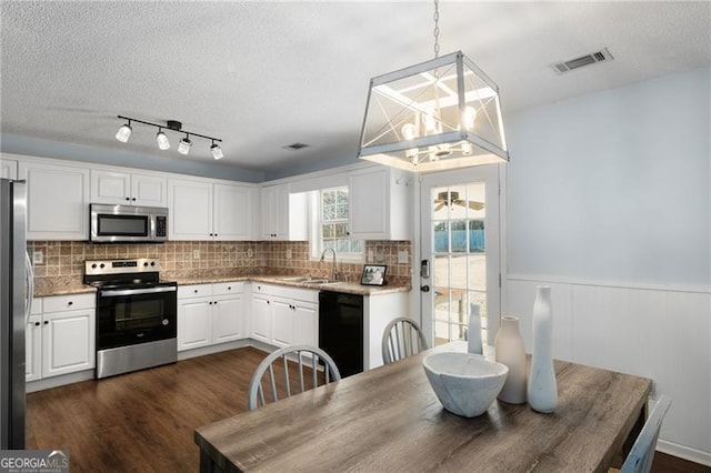 kitchen with pendant lighting, stainless steel appliances, visible vents, white cabinetry, and a sink