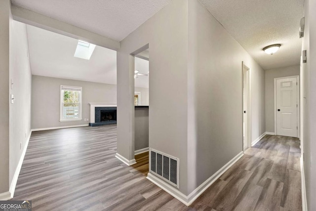 hallway with wood finished floors, visible vents, and baseboards