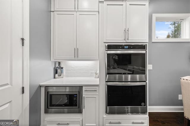 kitchen with tasteful backsplash, dark wood-style floors, appliances with stainless steel finishes, light countertops, and white cabinetry