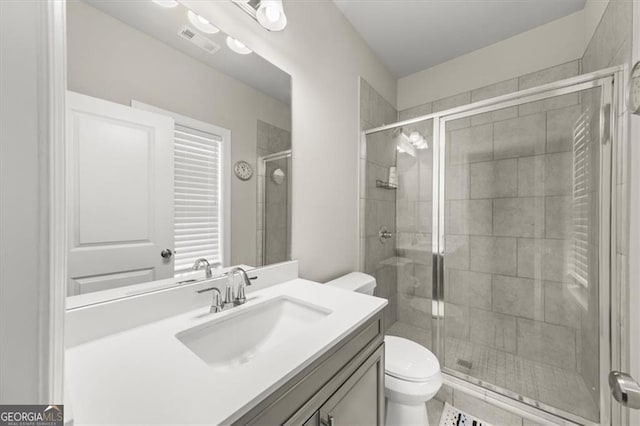 full bathroom featuring toilet, vanity, a shower stall, and visible vents