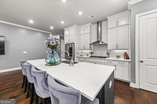 kitchen featuring wall chimney exhaust hood, a sink, a center island with sink, and stainless steel appliances