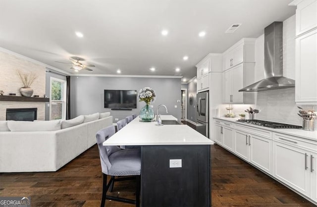 kitchen featuring open floor plan, light countertops, a center island with sink, and wall chimney exhaust hood