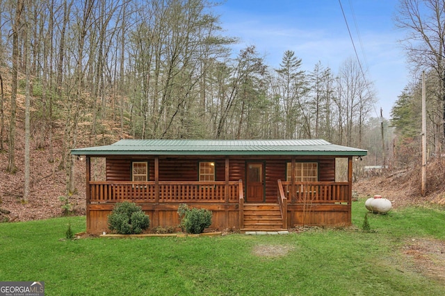 view of front of home featuring metal roof, a front lawn, log veneer siding, and a wooded view