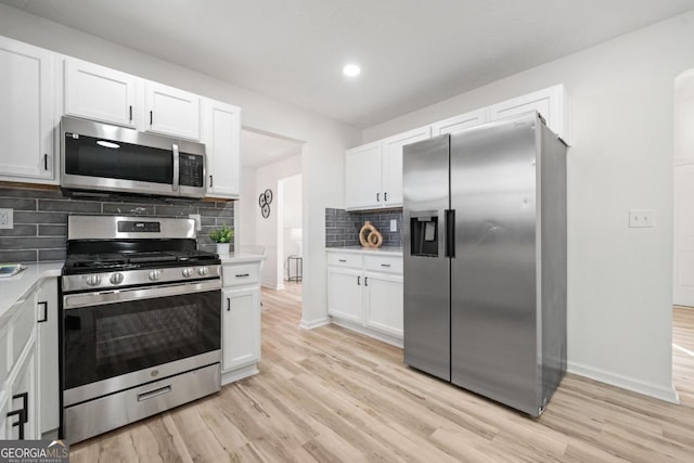 kitchen with light countertops, backsplash, appliances with stainless steel finishes, light wood-style floors, and white cabinets