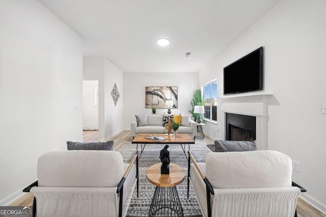 living area featuring baseboards, a fireplace, visible vents, and light wood-style floors