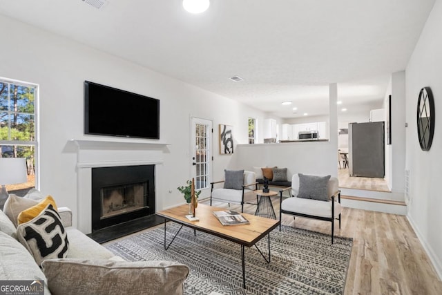 living area with light wood-style flooring, recessed lighting, a fireplace with flush hearth, visible vents, and baseboards