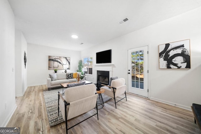 living area featuring light wood-type flooring, visible vents, a fireplace, and baseboards